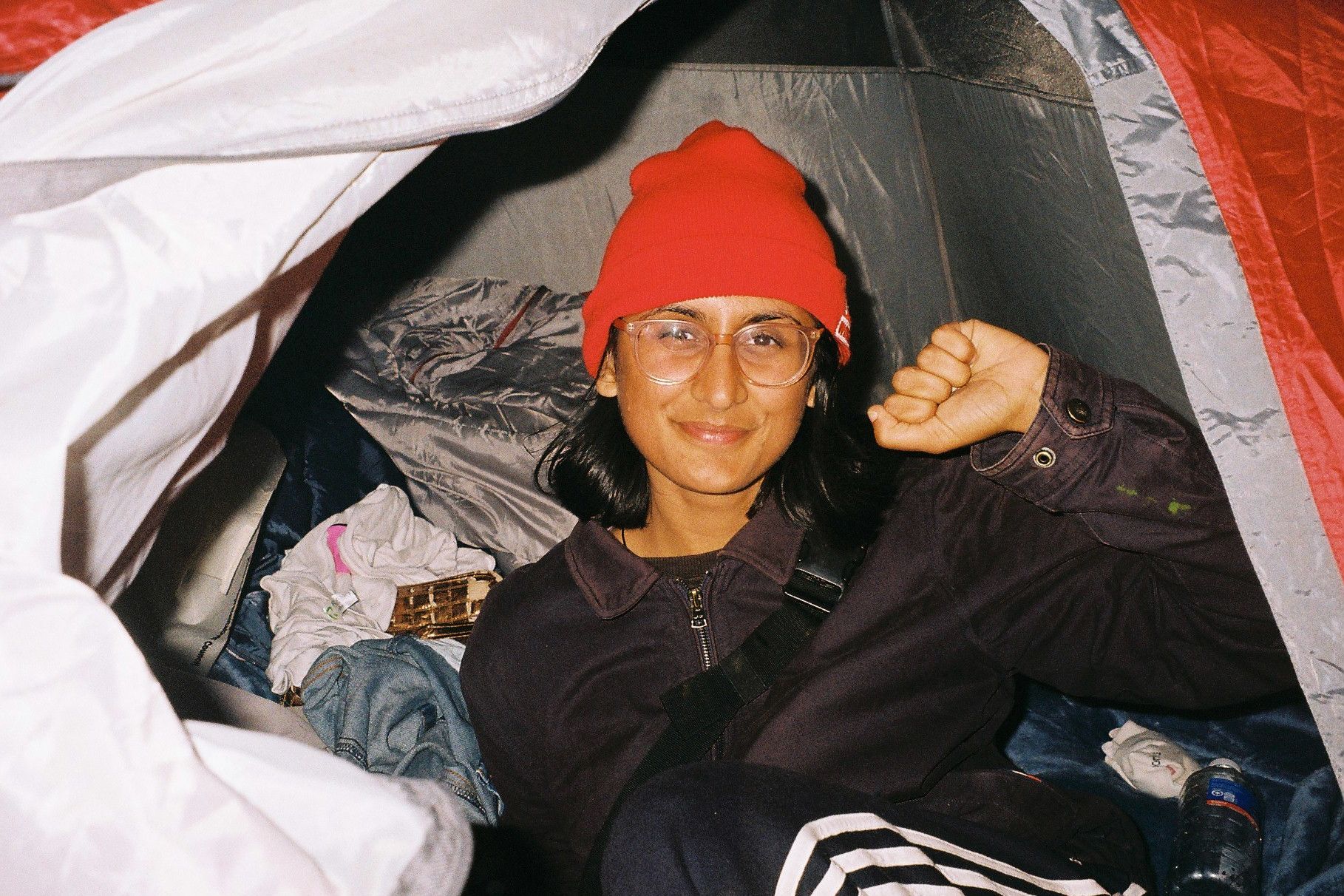 A person wearing a red beanie holding her fist up while in a tent